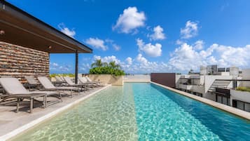 A rooftop pool with clear blue water, surrounded by lounge chairs and a modern building facade.