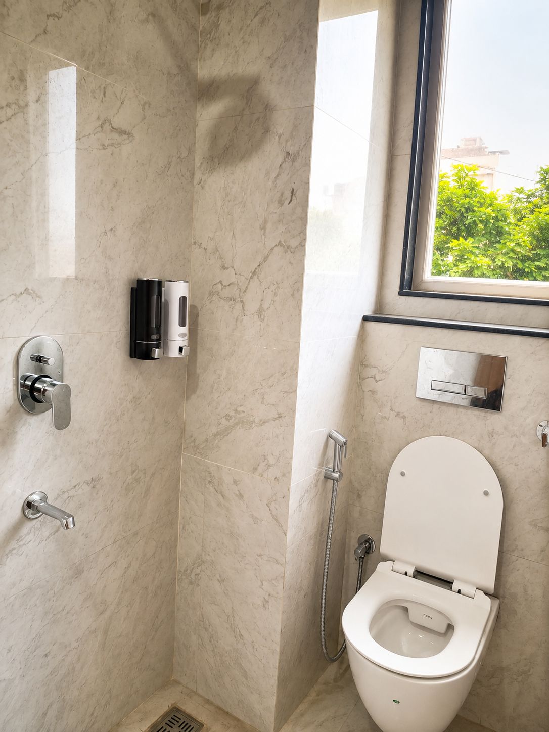 A bathroom with a shower, toilet, and a window with a view of greenery.