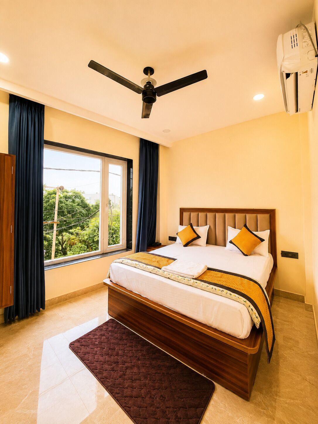 Habitación de hotel con una cama, ventilador de techo, ventana con cortinas y un equipo de aire acondicionado.