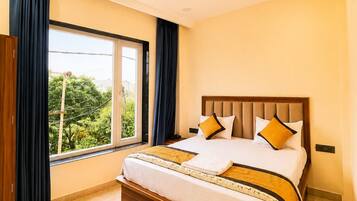 Habitación de hotel con una cama, ventilador de techo, ventana con cortinas y un equipo de aire acondicionado.