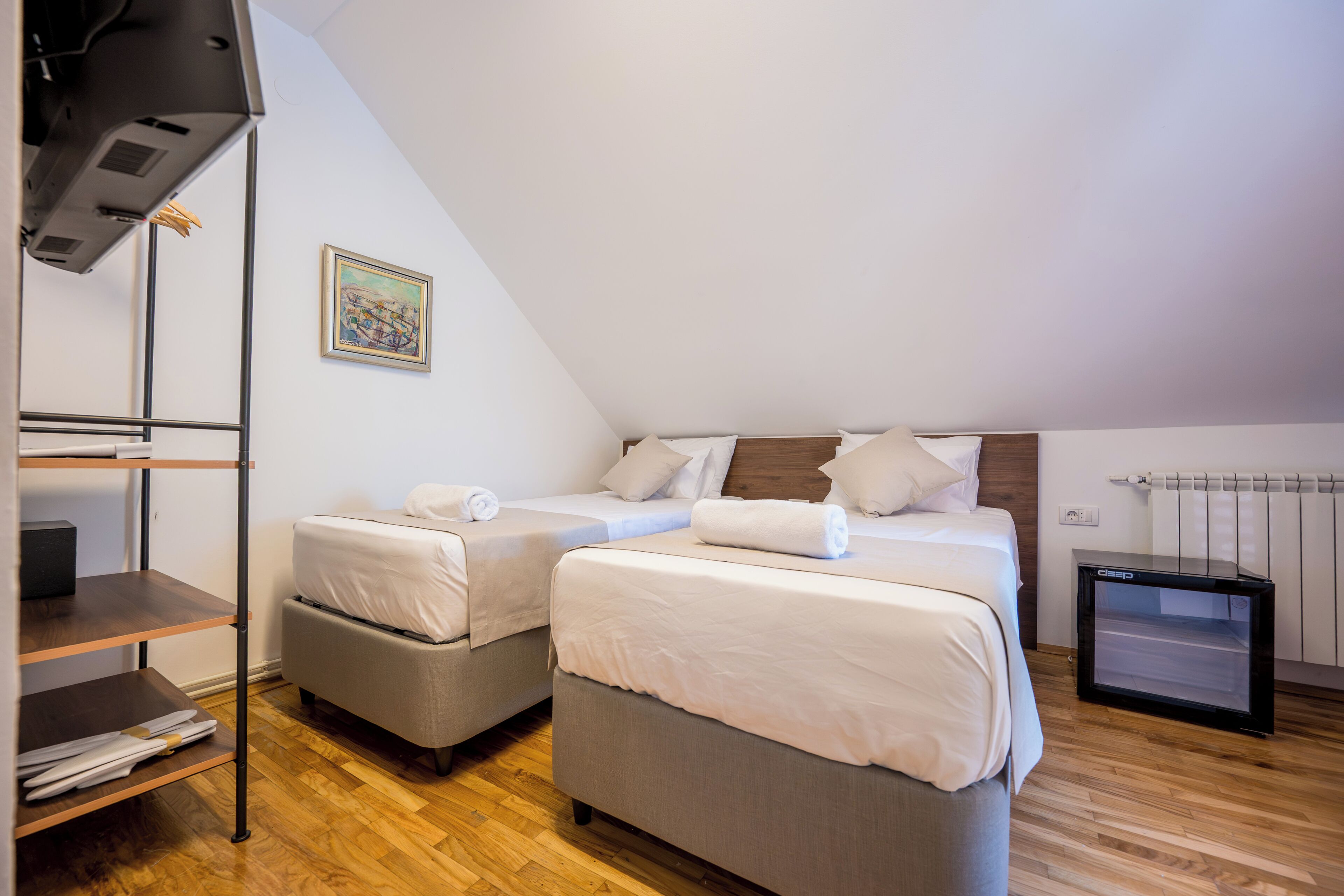 A hotel room with two beds, a wooden floor, a radiator, and a painting on the wall.
