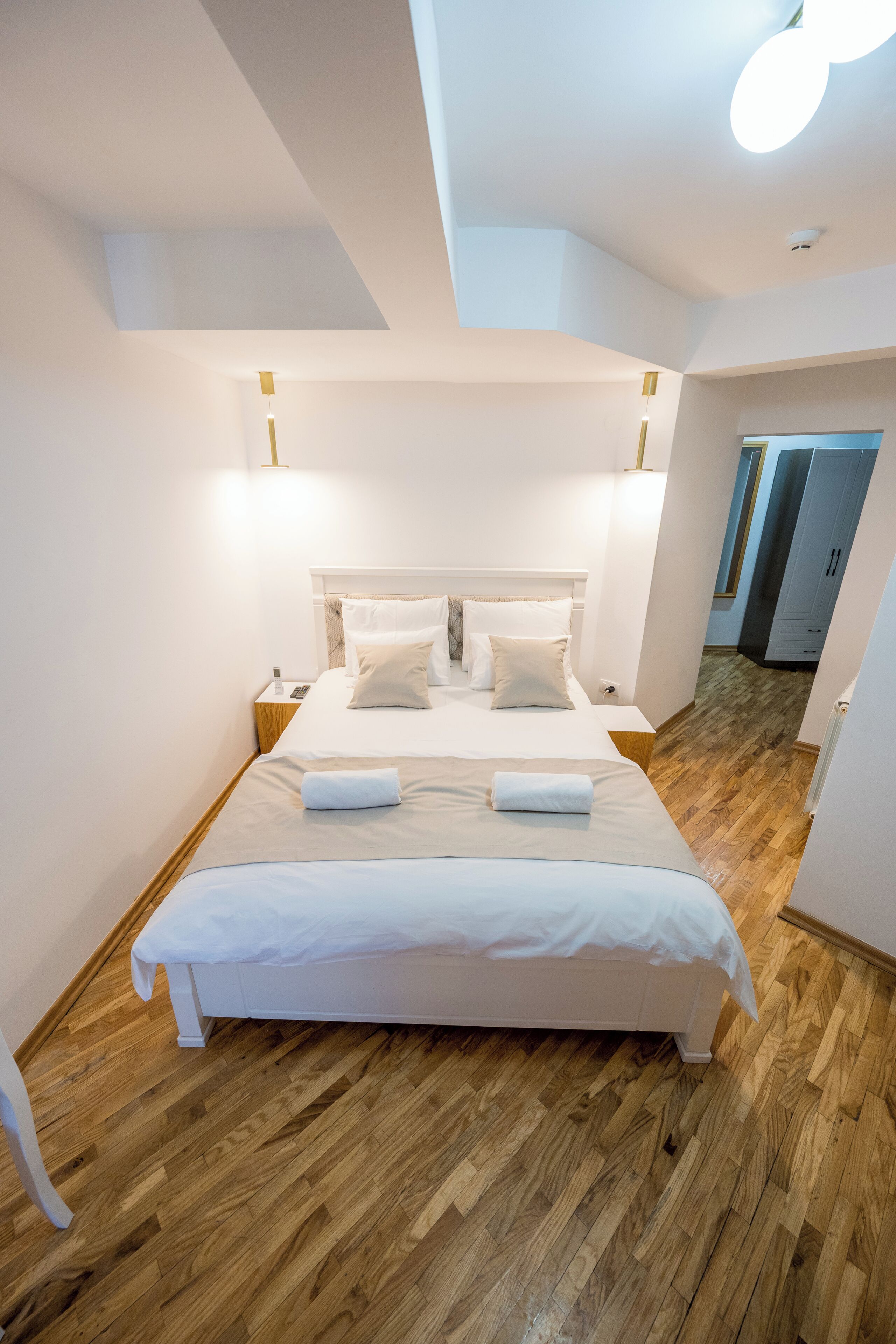 A modern hotel room with a large bed, wooden flooring, and a view of the hallway.