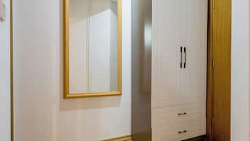 A room with a wooden floor, a wardrobe with multiple drawers, a mirror on the wall, and a door.