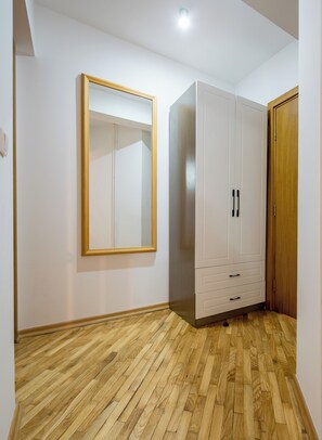 A room with a wooden floor, a wardrobe with multiple drawers, a mirror on the wall, and a door.