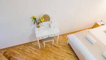 Ein Schlafzimmer mit Holzboden, einem Bett mit weißer Bettwäsche, einem kleinen weißen Nachttisch mit Blumen in einer Vase und einem runden Spiegel.
