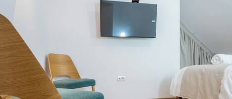 A modern bedroom with a wooden floor, a bed, a chair, and a flat-screen TV mounted on the wall.