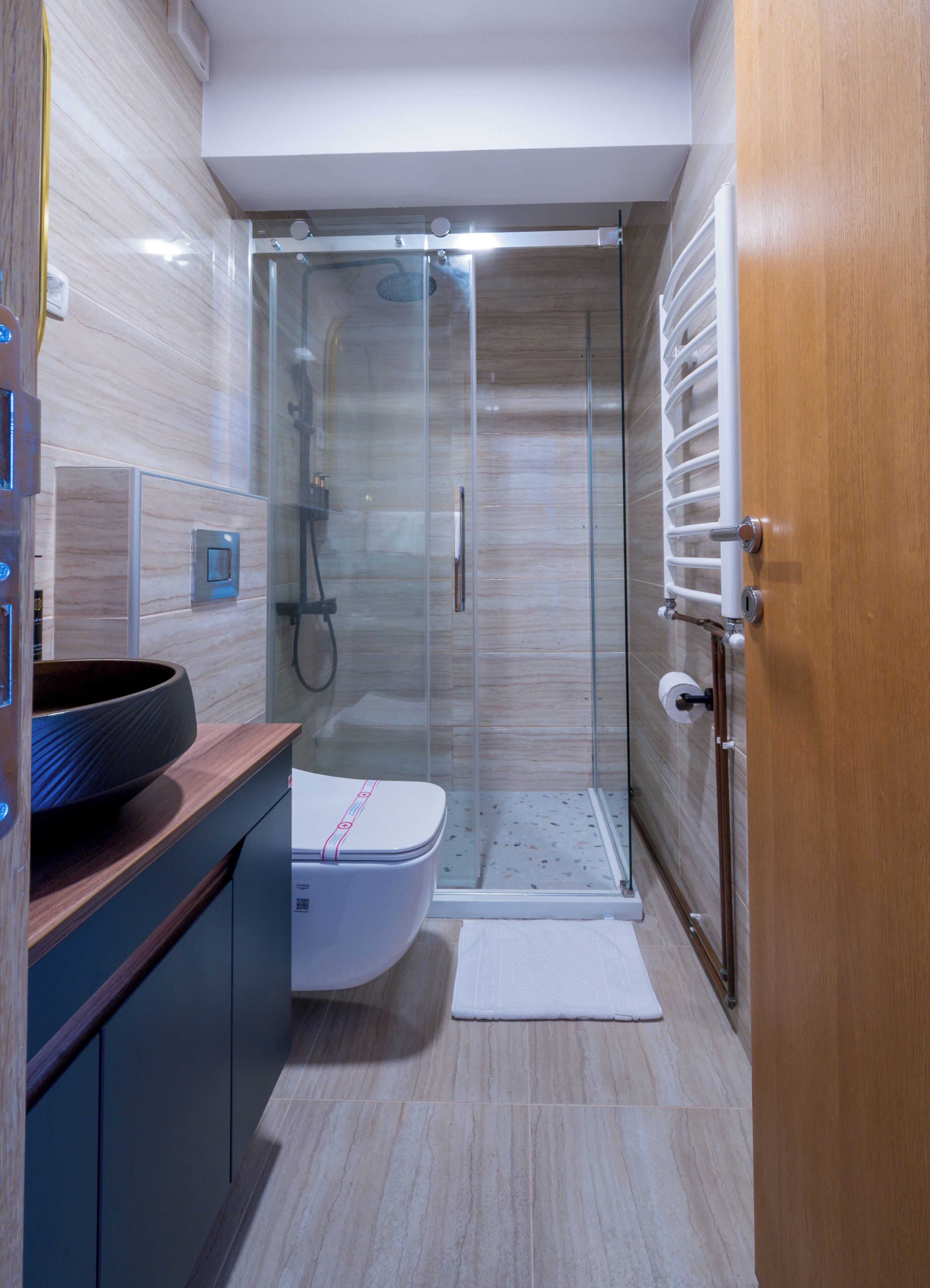 A modern bathroom with a glass-enclosed shower, a toilet, and a wooden vanity.