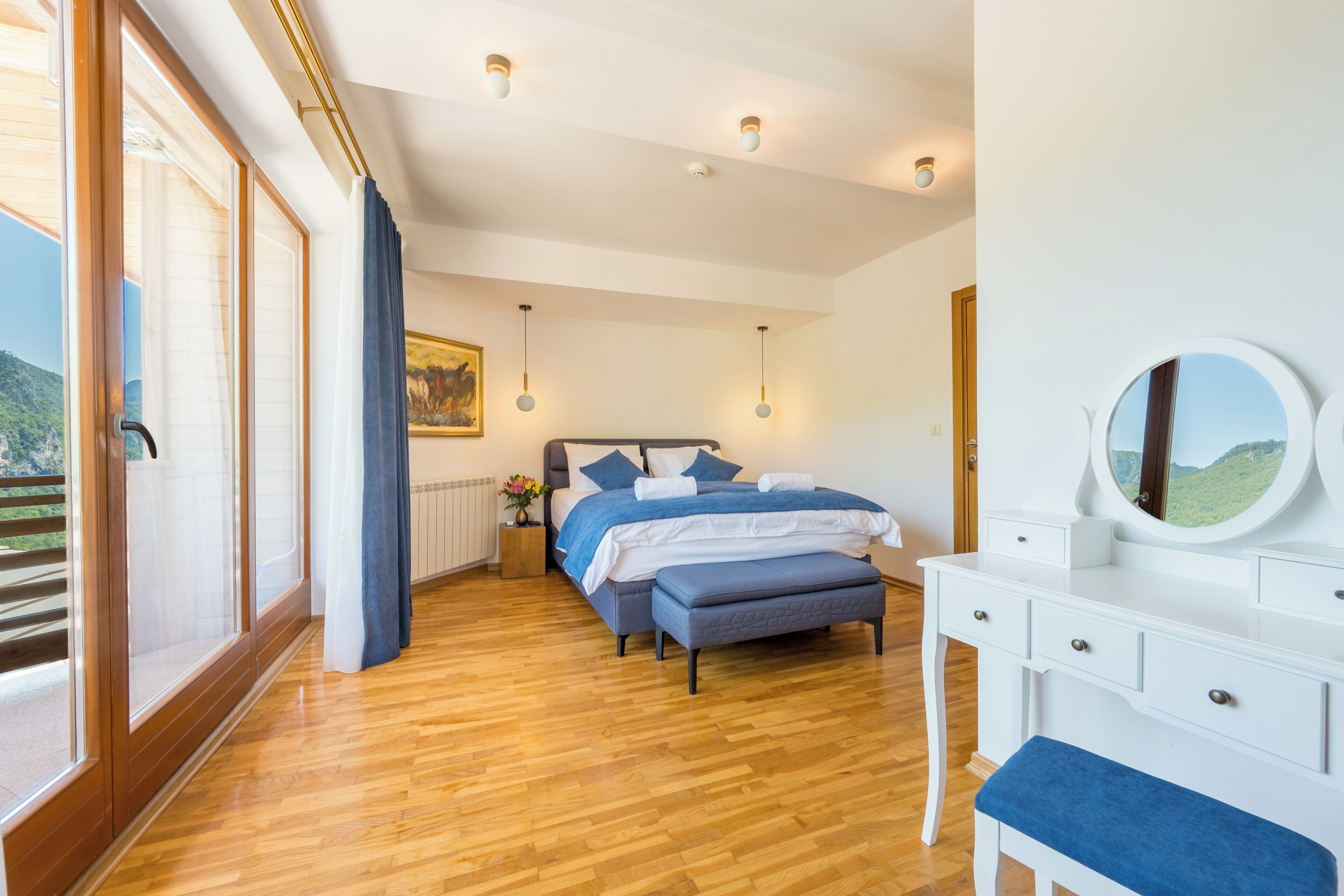 Une chambre à coucher comprenant un lit, une table de chevet, une commode et une grande fenêtre donnant sur un beau paysage.