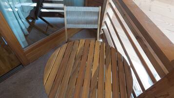 Una terraza de madera con una mesa redonda y una silla, un vidrio y vista al interior.