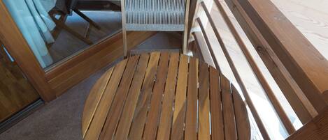 A wooden deck with a round table and a chair, a glass door, and a view of the interior.