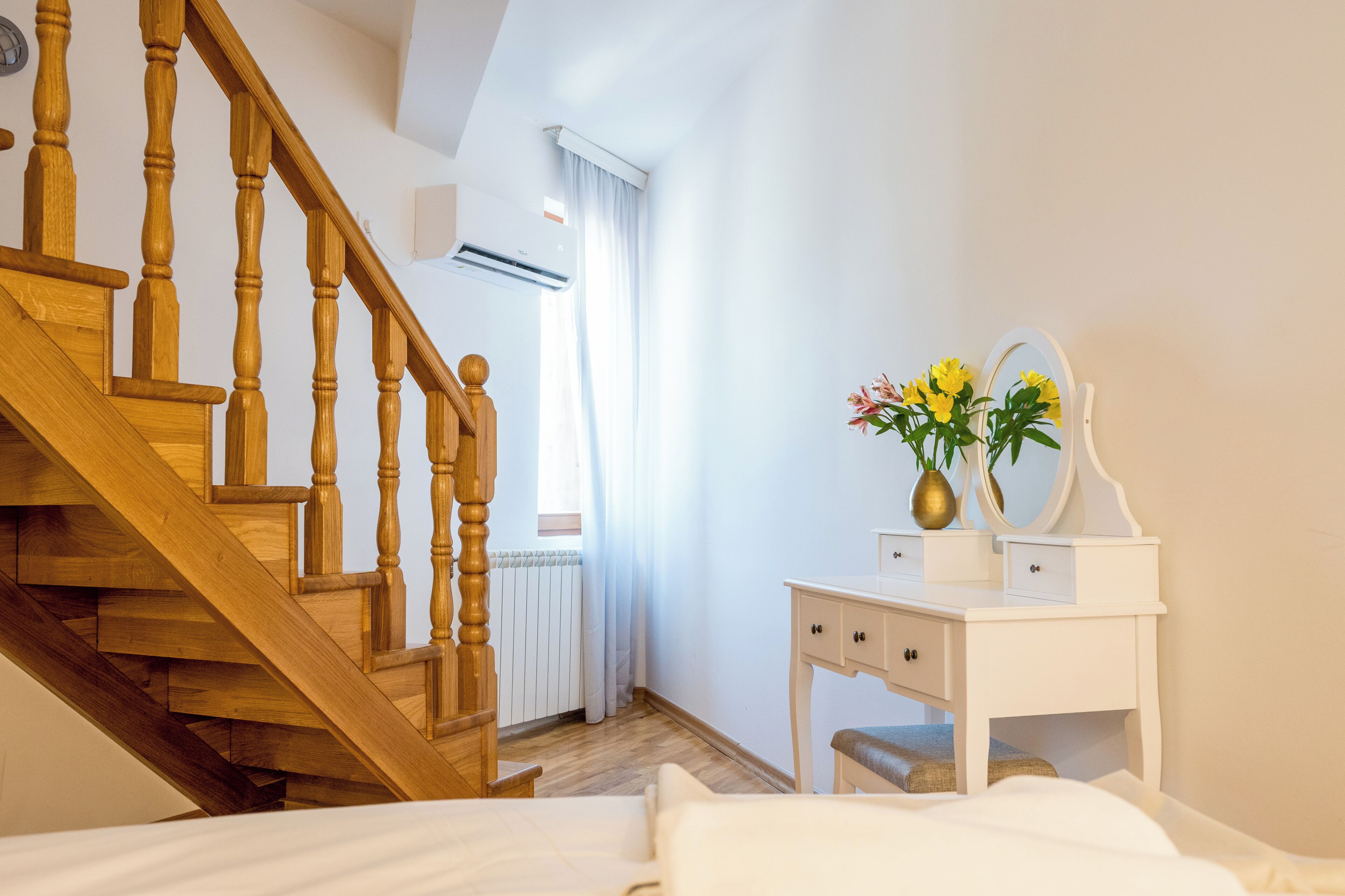 Ein Schlafzimmer mit einer Holztreppe, einem weißen Nachttisch mit Spiegel und Blumen sowie einer Heizung.