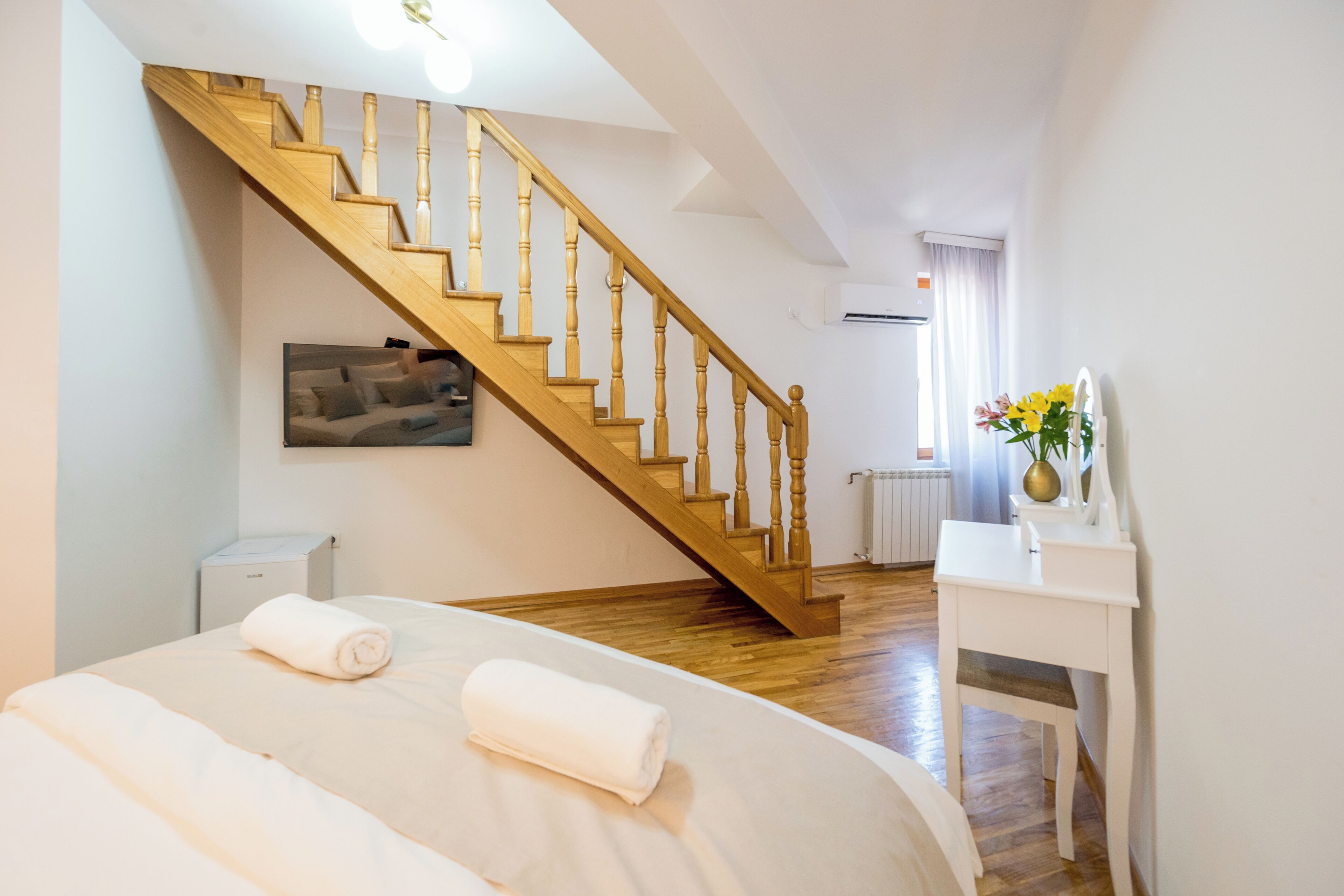 Un dormitorio con escalera de madera, una cama con ropa blanca, una mesita de noche y un radiador.