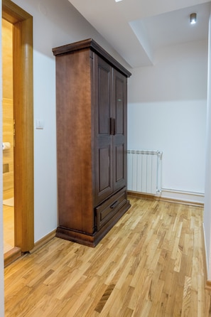 A room with a wooden floor, a dark wooden wardrobe, and a white radiator.