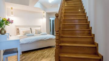 Una escalera conduce a un dormitorio con cama, un escritorio y un florero con flores.