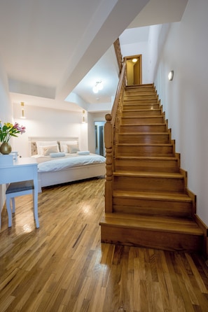 Una escalera conduce a un dormitorio con cama, un escritorio y un florero con flores.