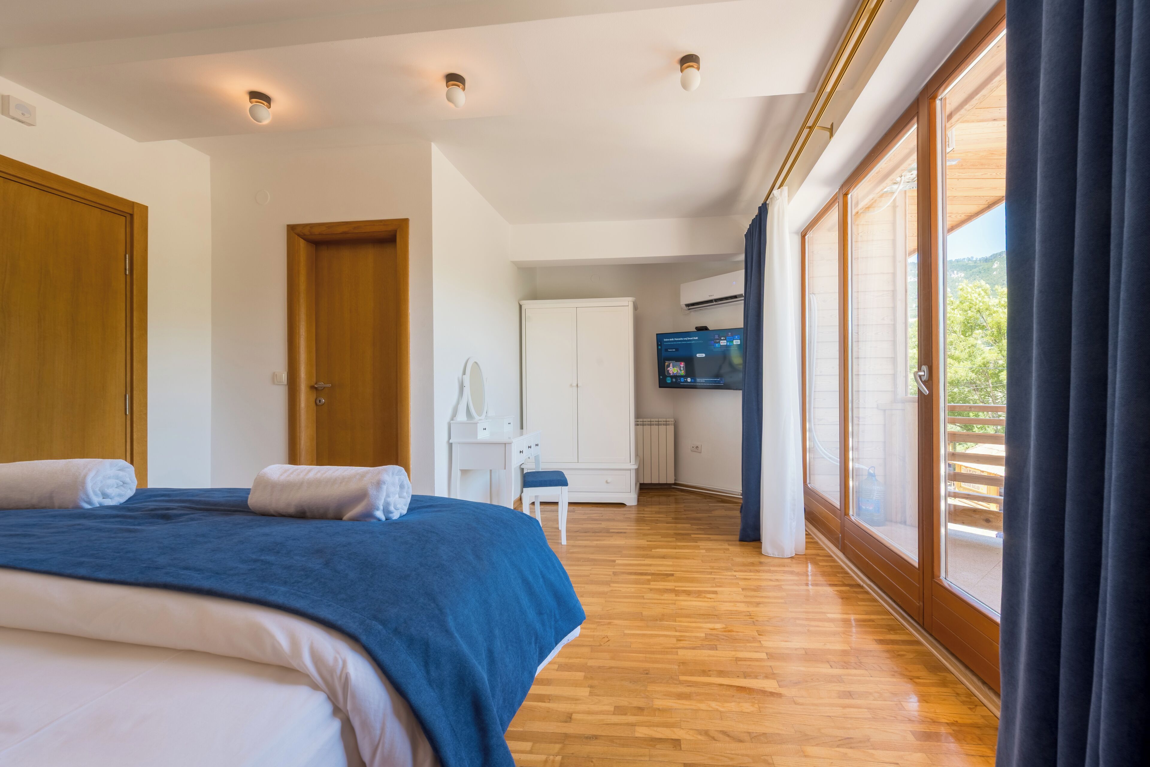 Un dormitorio con una cama grande, un armario de madera, un escritorio con una silla y una televisión.