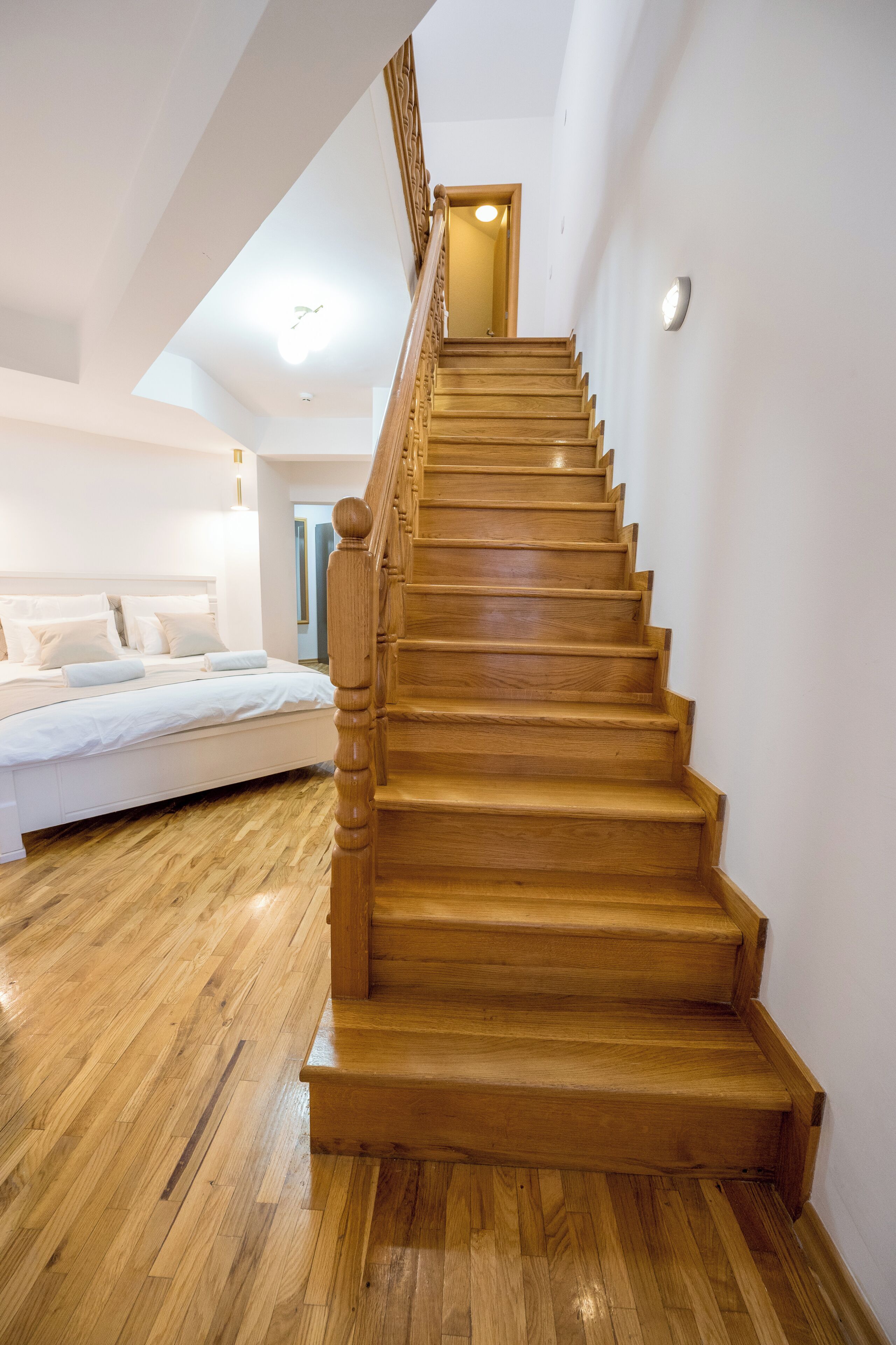 Una escalera de madera que lleva a un dormitorio con una cama y una mesita de noche.