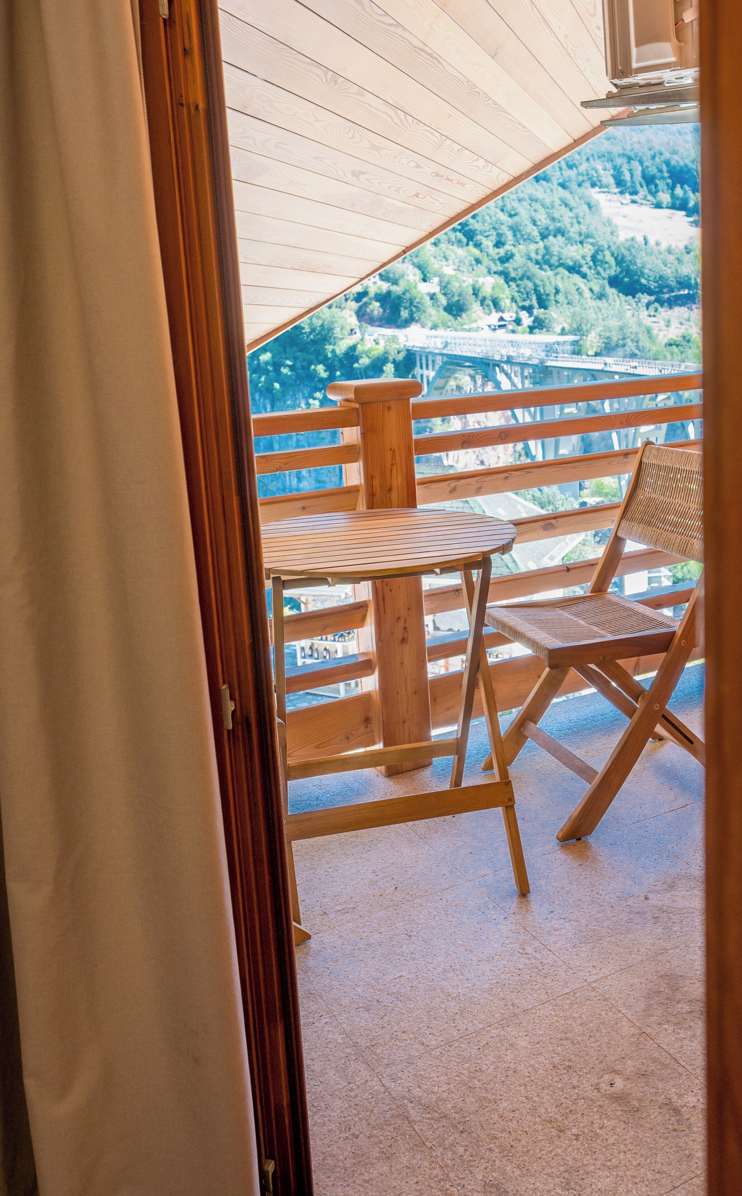 An outdoor wooden deck with a table and a chair, overlooking a forested landscape.