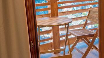 An outdoor wooden deck with a table and a chair, overlooking a forested landscape.