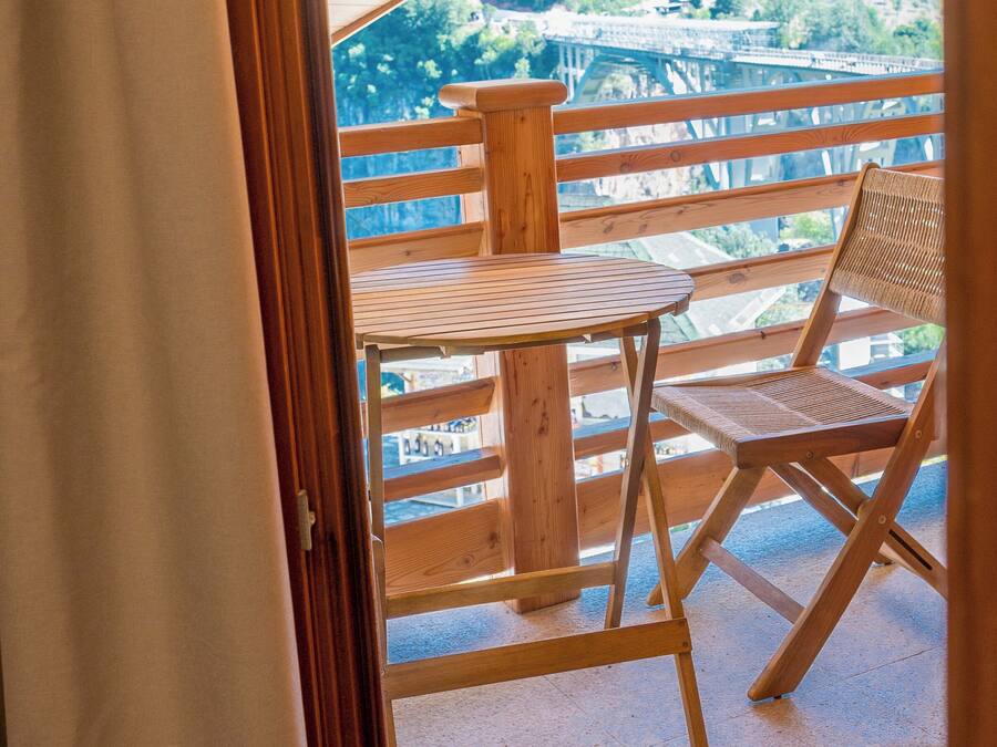 Una terraza de madera al aire libre con una mesa y una silla, con vistas a un paisaje boscoso.