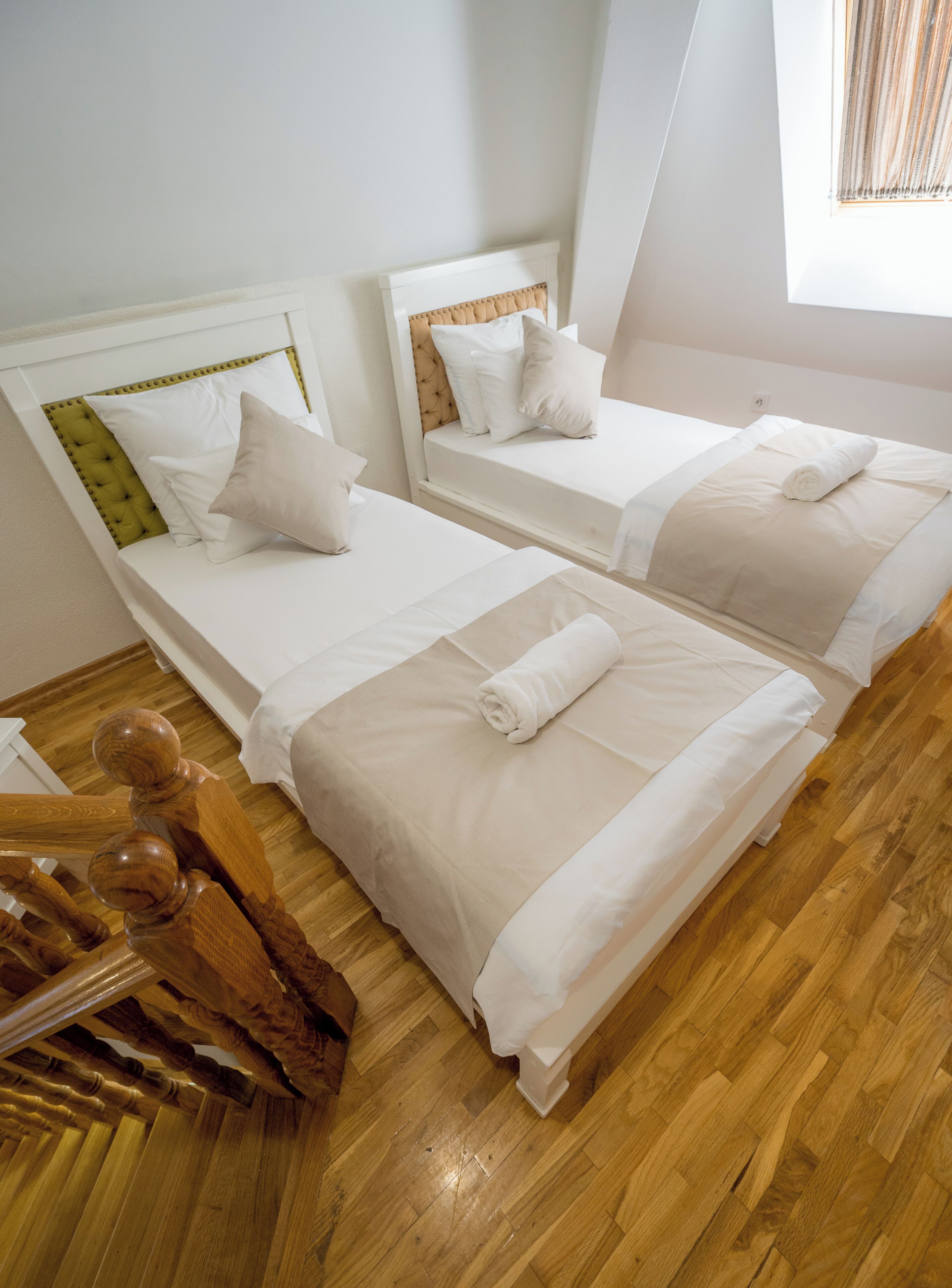 A hotel room with two beds, wooden flooring, and a window with blinds.