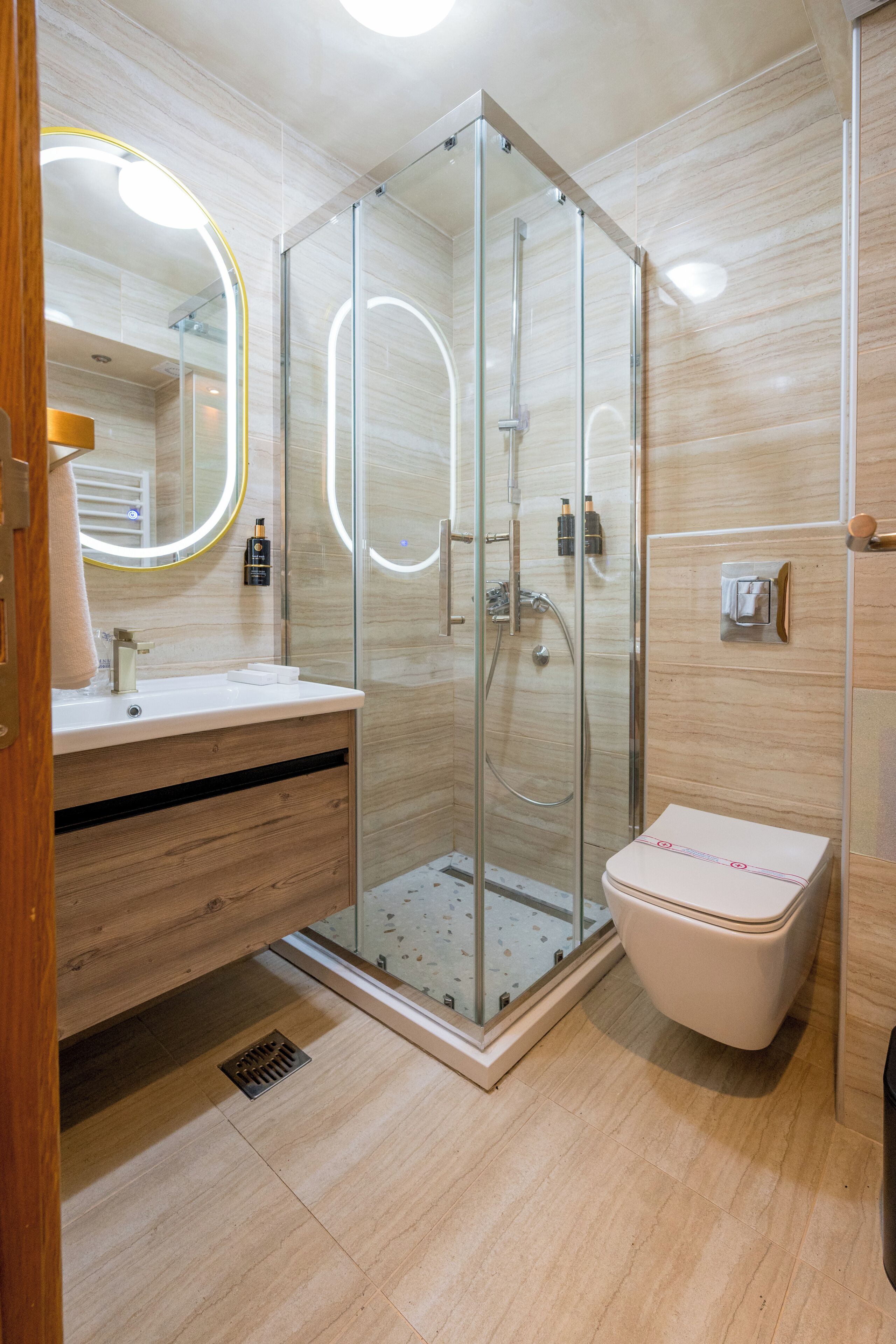 Een moderne badkamer met een douchecabine van glas, een houten wastafelmeubel en een wit toilet.