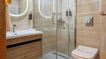 Een moderne badkamer met een douchecabine van glas, een houten wastafelmeubel en een wit toilet.