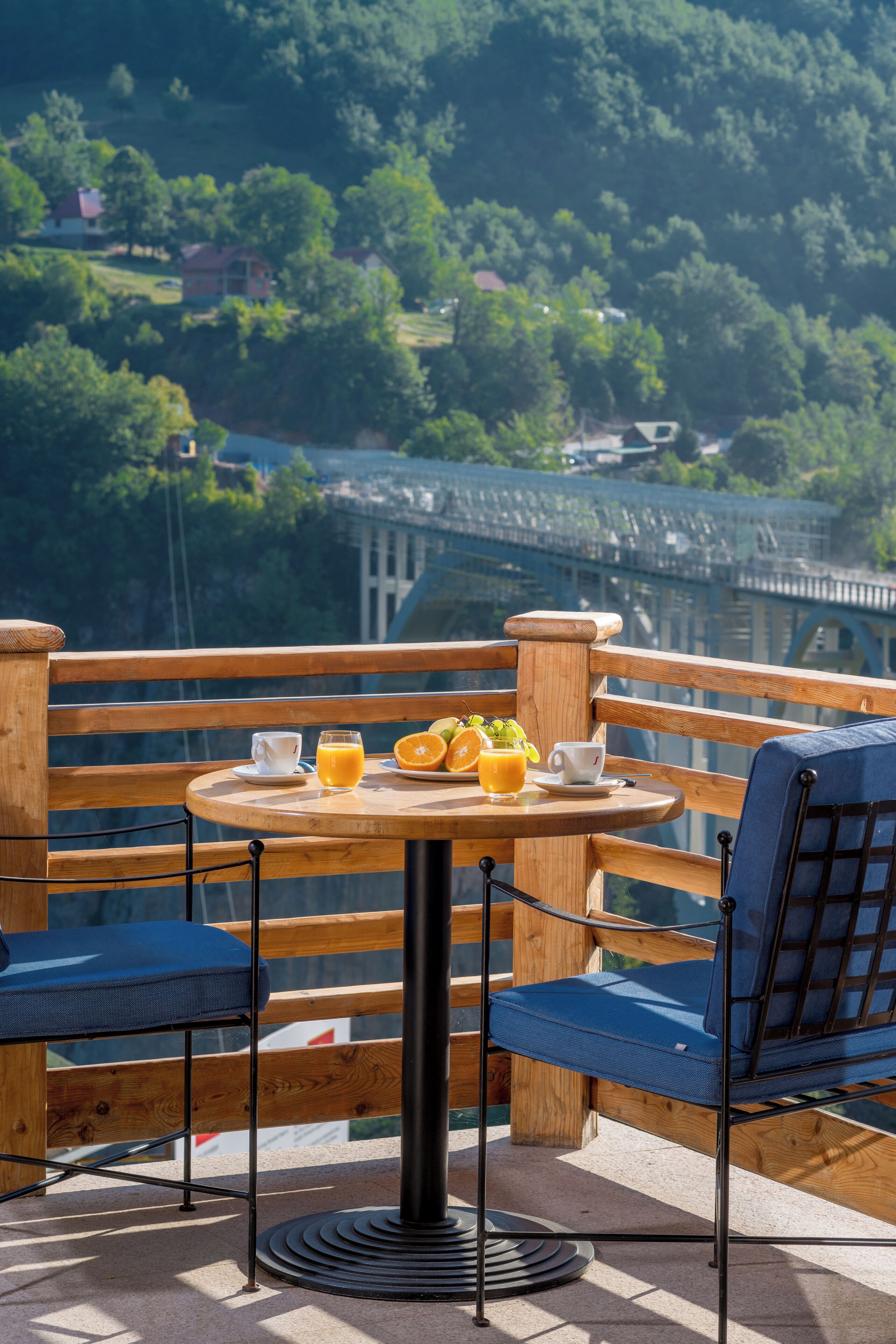 A terrace with a table set for breakfast, overlooking a bridge and greenery.