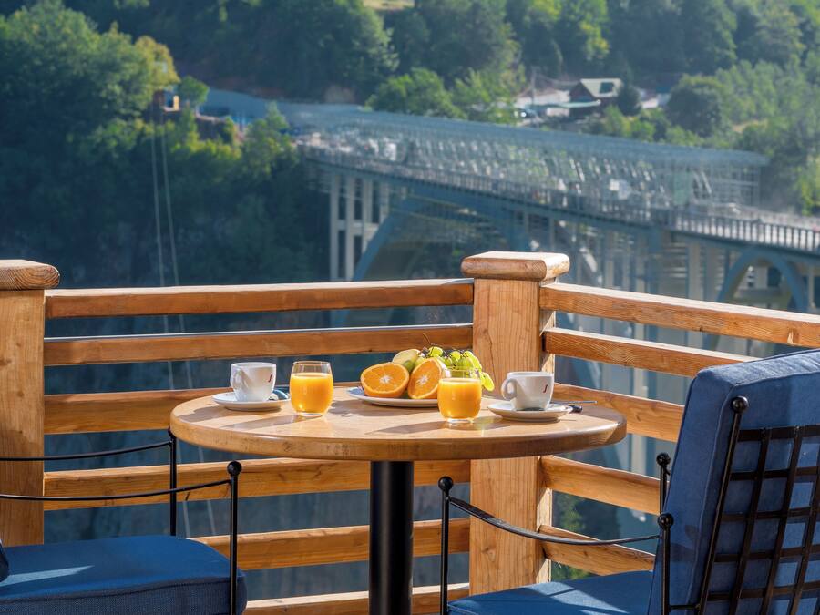 Una terrazza con un tavolo apparecchiato per la colazione, vista su un ponte e sulla vegetazione.