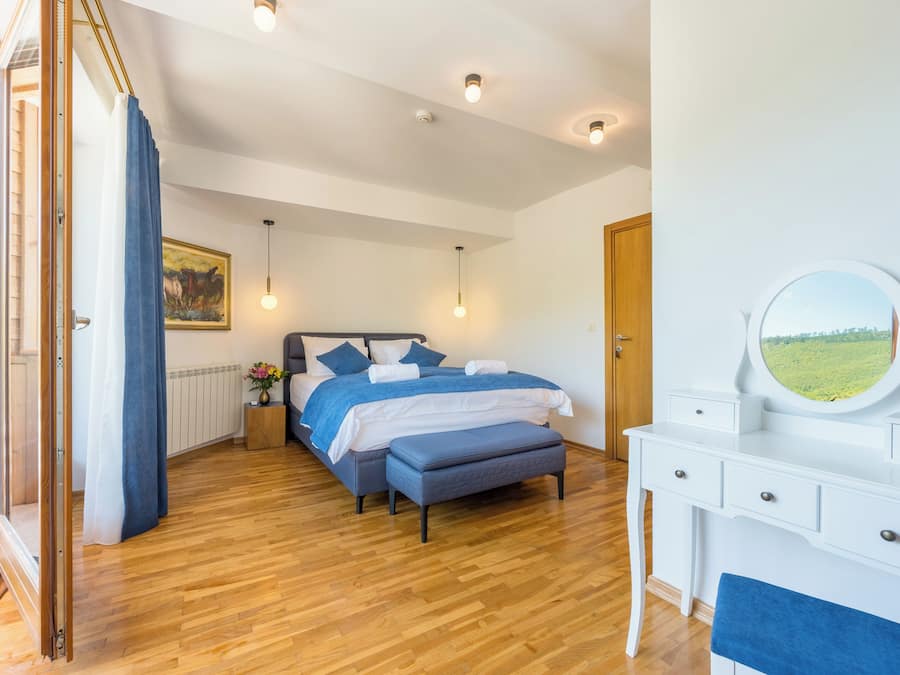 A bedroom with a bed, bedside table, dresser, and a view of a green landscape.