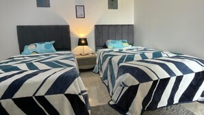 Una habitación de hotel con dos camas, una mesita de noche, una lámpara y una pequeña mesa.
