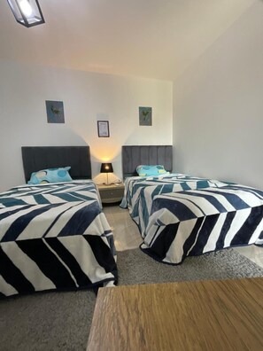 A hotel room with two beds, a nightstand, a lamp, and a small table. - Terrific 3-bedroom apartment with AC and Free-Wifi in lovely Madinty Garden View (Madinaty)