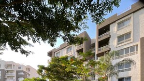 Un edificio residencial de varios pisos con balcones, rodeado de follaje cuidado y un sendero pavimentado.