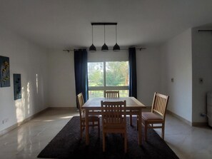 Ett matrum med ett bord och stolar, ett fönster med gardiner och en taklampa.