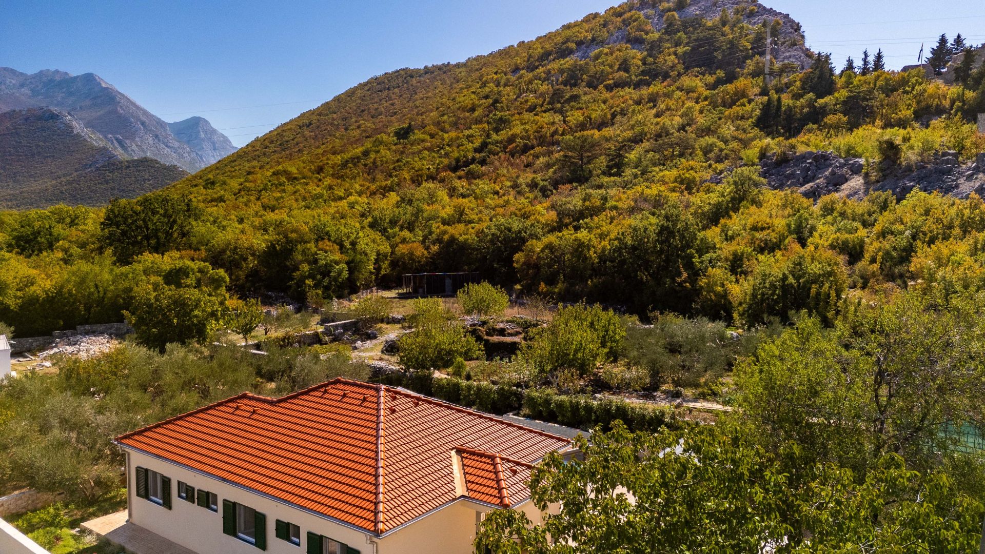 Ein Haus mit rotem Ziegeldach, umgeben von Bäumen und einer Berglandschaft.