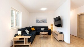 Ein modernes Wohnzimmer mit einer schwarzen Couch, einem runden Couchtisch, einem an der Wand montierten Fernseher und einer Holzkabine.