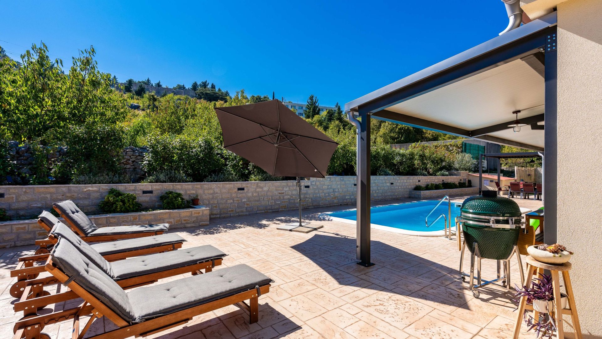 Zona de piscina amb gandules, una barbacoa i una zona d'estar coberta.