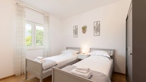 Ein Schlafzimmer mit zwei Einzelbetten, einem Fenster mit Vorhängen und Wandbildern.
