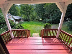 A covered wooden deck with a view of a green lawn and a house in the background. - Creekfront • Pet Friendly • Sleeps 4 • Near Boone & West Jefferson (Todd)