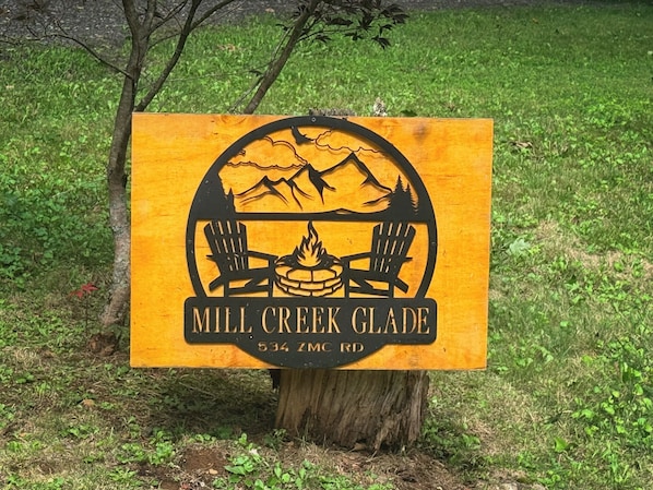 Un panneau indiquant l’emplacement de Mill Creek Glade, avec une illustration représentant une montagne et des chaises de camping, situé au 534, chemin ZMC.
