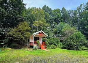 A small cabin with a porch and steps, surrounded by dense trees and grass. - Creekfront • Pet Friendly • Sleeps 4 • Near Boone & West Jefferson (Todd)