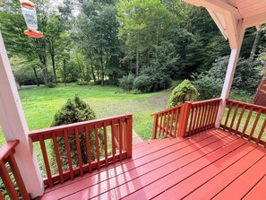 Um deck de madeira com guarda-corpo vermelho, com vista para um gramado com árvores.
