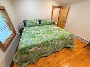 Um quarto com uma cama, uma janela com persianas, uma porta e piso de madeira.