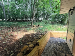 Um deck de madeira com um muro de suporte de pedra, rodeado por uma área arborizada.