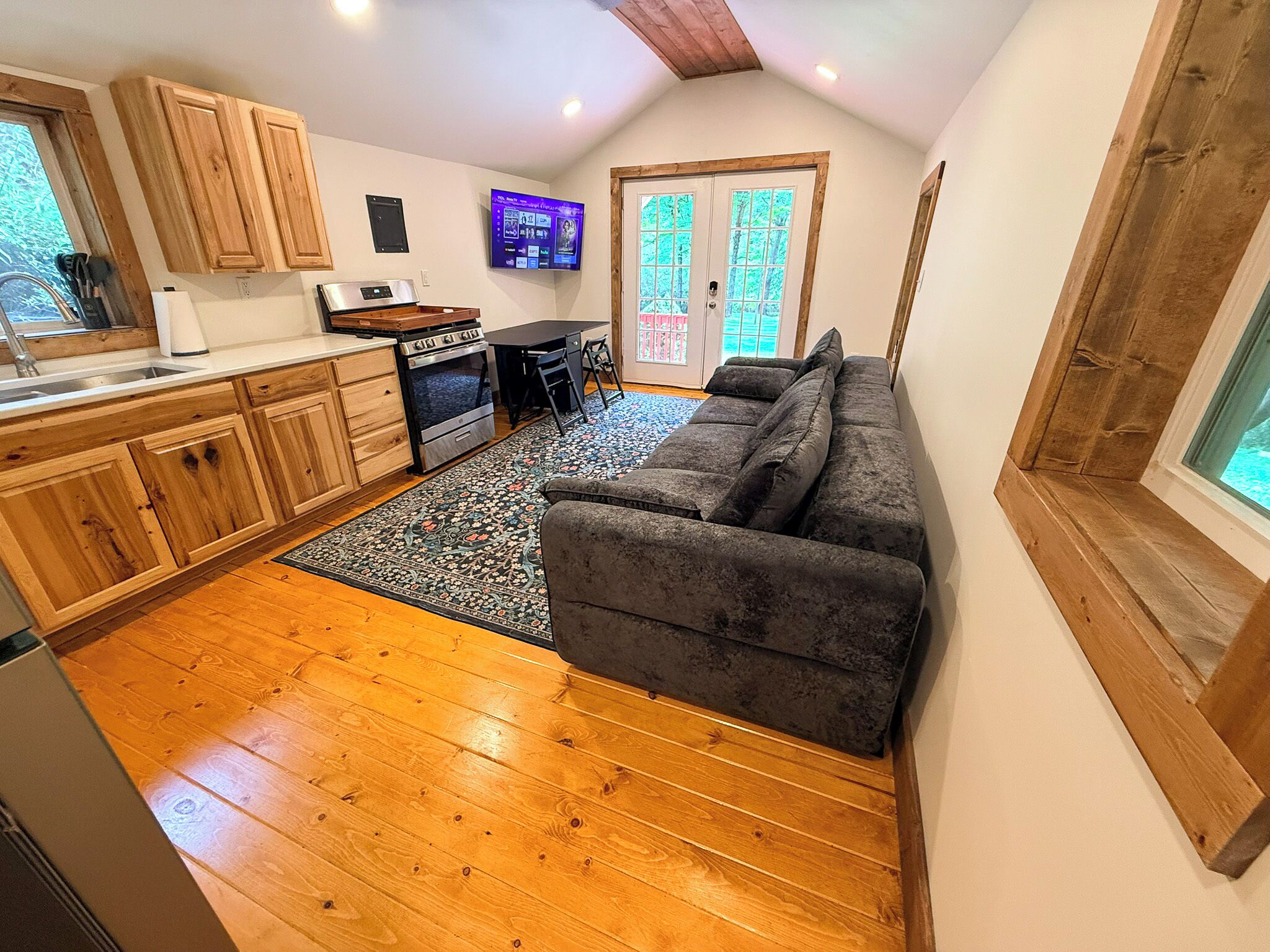 A compact kitchen with wooden cabinets, a built-in oven, and a dining area with a black table and chairs.