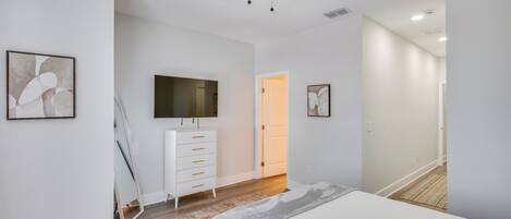 A bedroom with a bed, a dresser, a ceiling fan, and artwork on the walls.