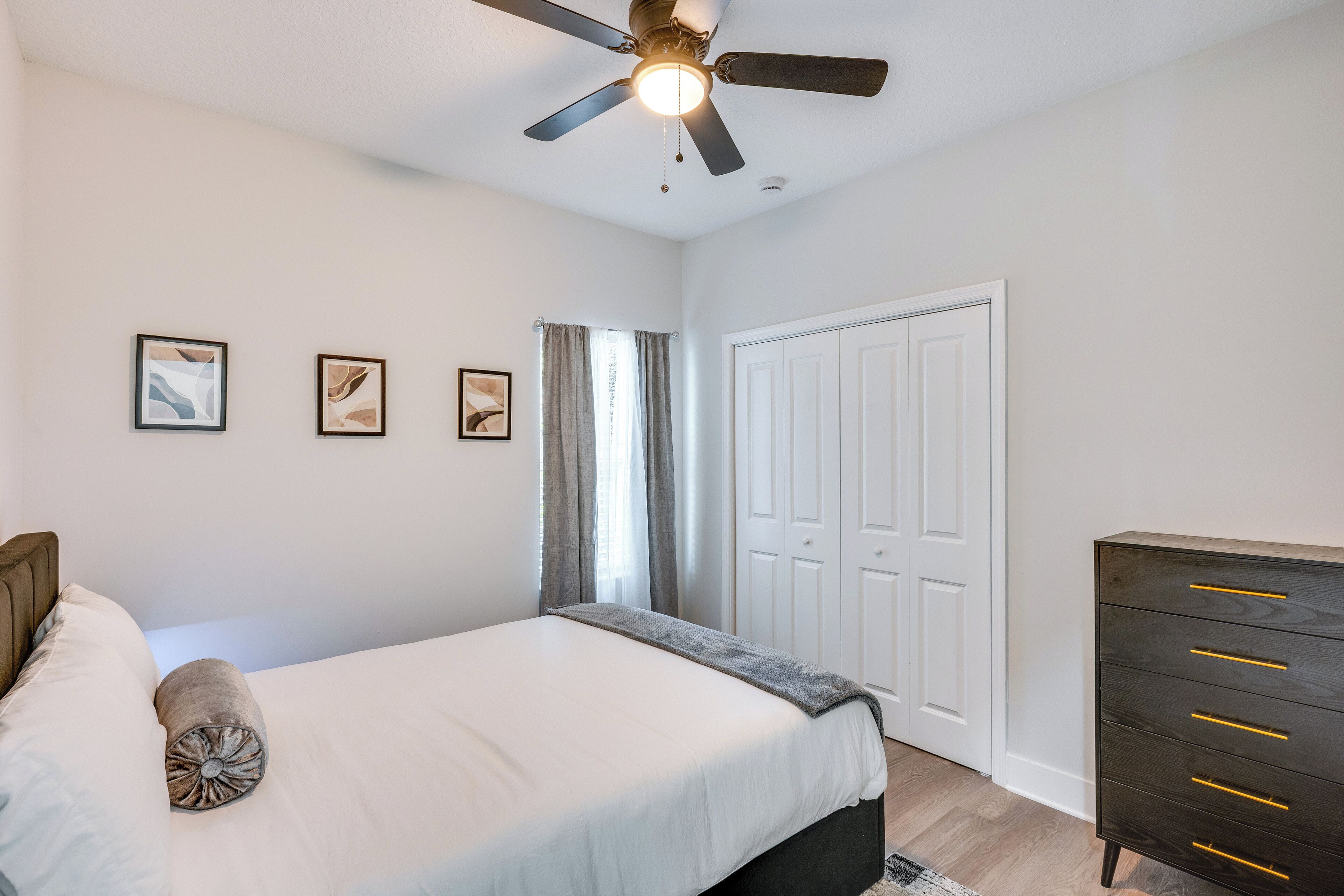 Un dormitorio con cama, ventilador de techo, cómoda y puerta.