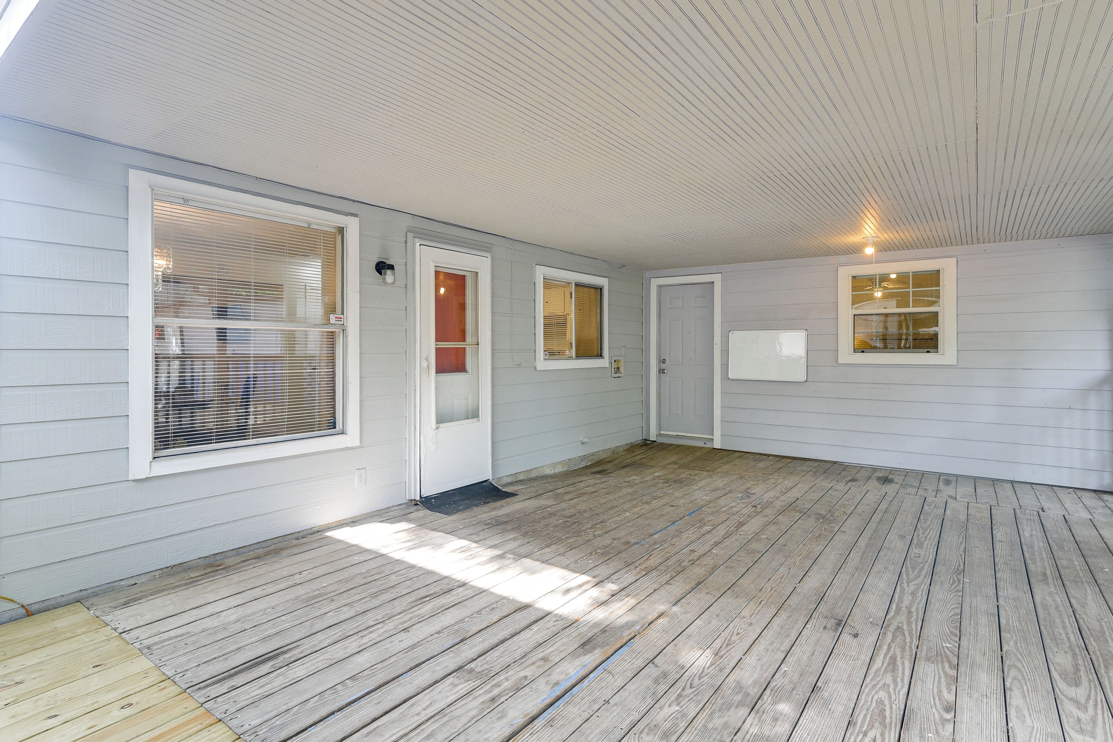 A covered porch with a wooden floor, white exterior walls, and multiple windows with blinds.
