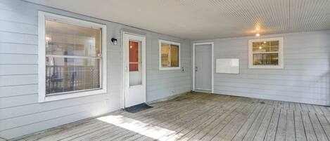 A covered porch with a wooden floor, white exterior walls, and multiple windows with blinds.