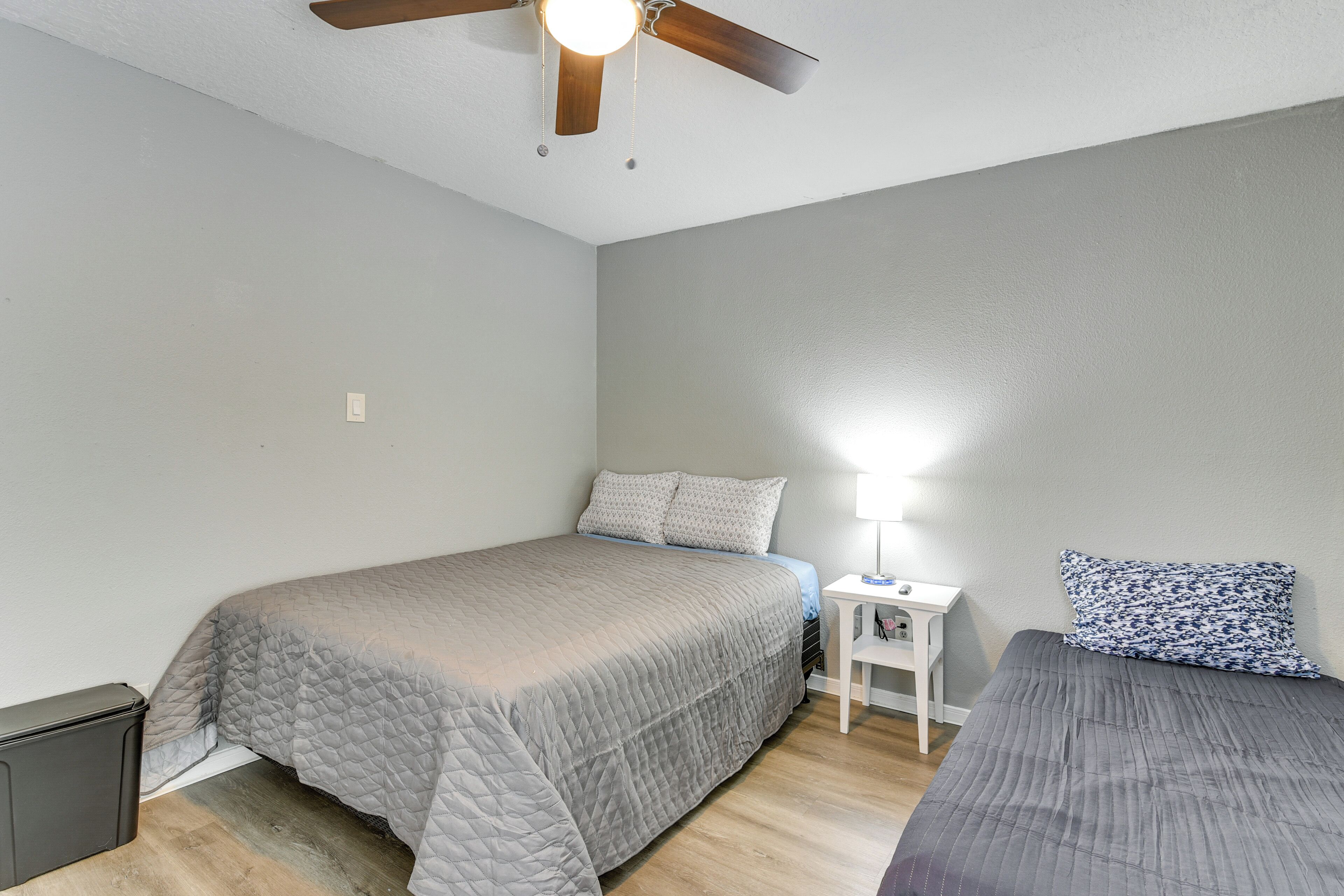 A bedroom with a bed, bedside table, lamp, and a ceiling fan.